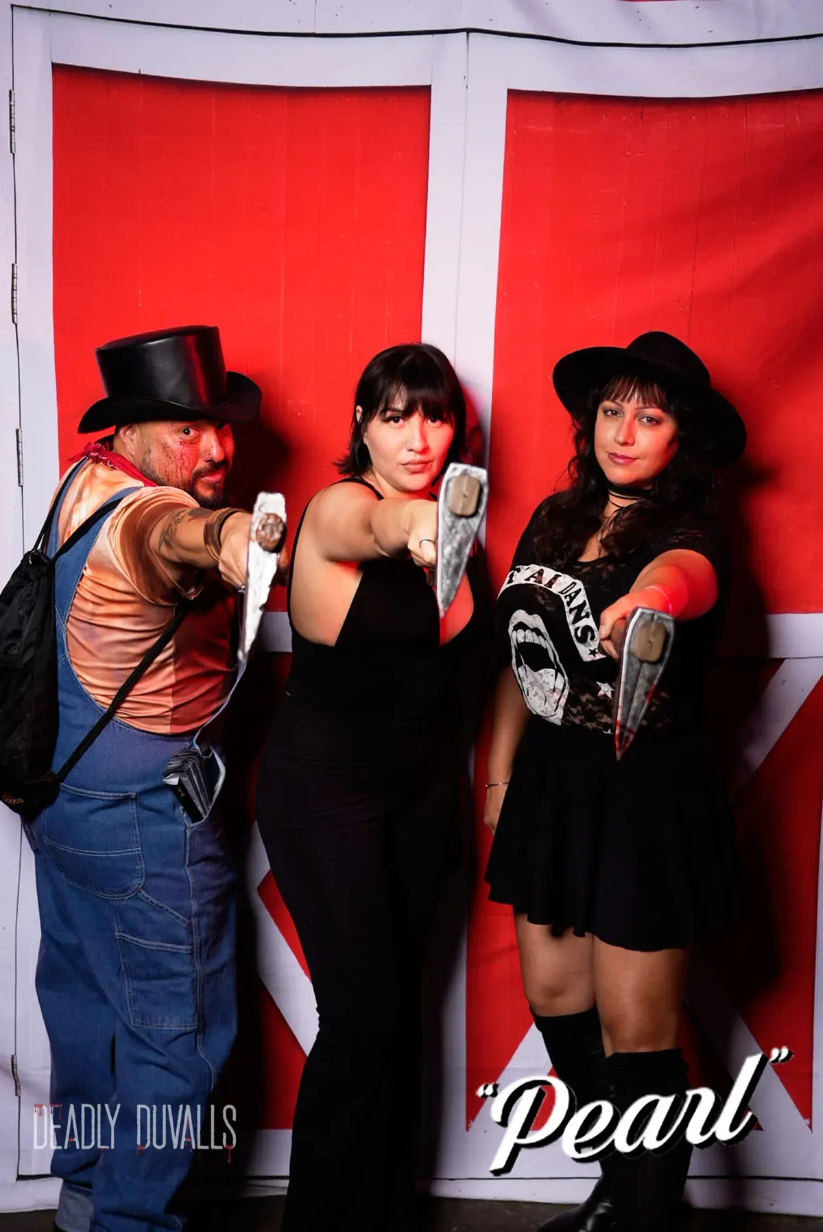 Three friends pointing prop knives at the camera in front of the red barn backdrop at the Deadly Duvalls Pearl event photo booth