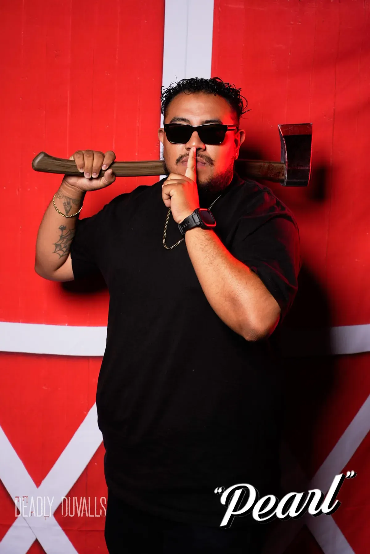 Guest in sunglasses balancing an axe across his shoulders with a finger to his lips at the Pearl themed photo booth in Los Angeles
