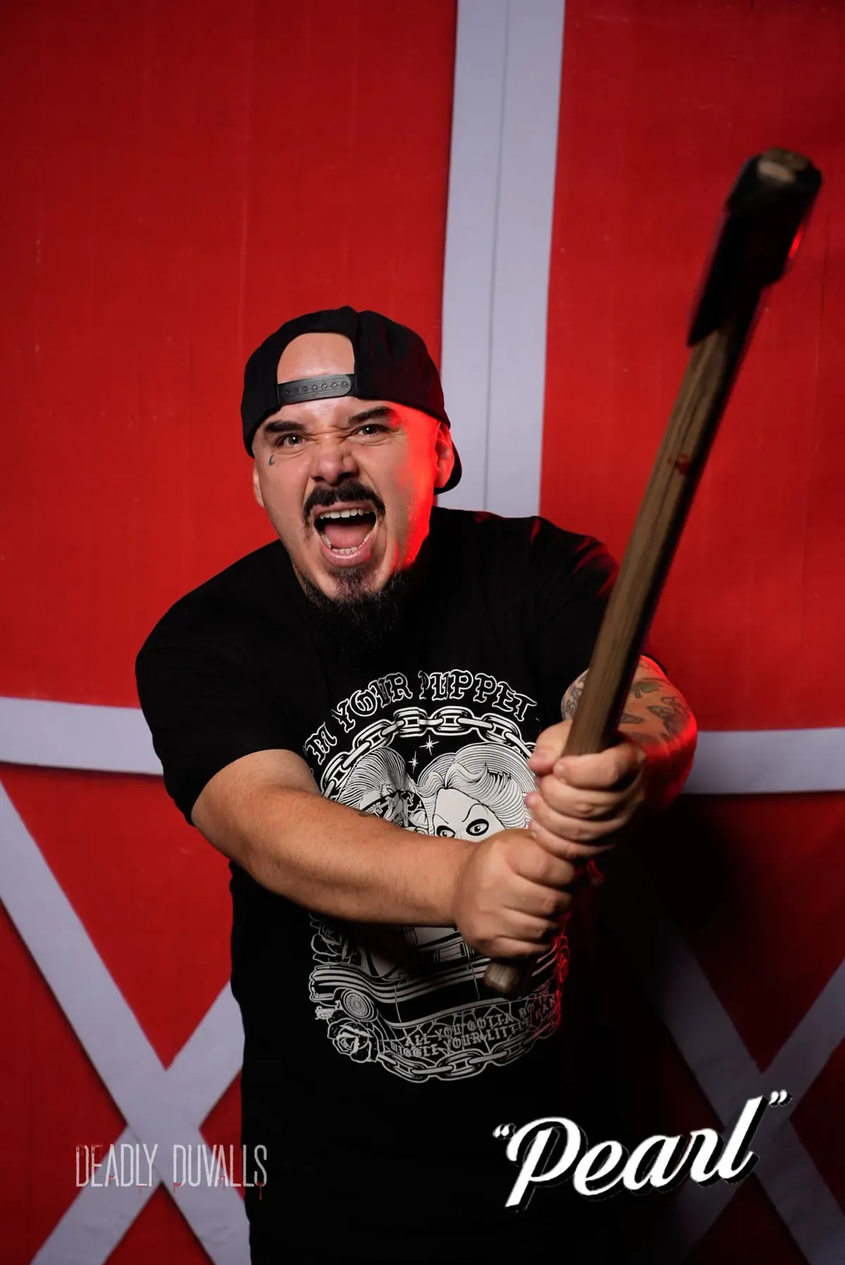 Guest in a backwards cap mid-yell, swinging a prop axe at the camera in front of the red barn backdrop — Pearl event photo booth, Los Angeles