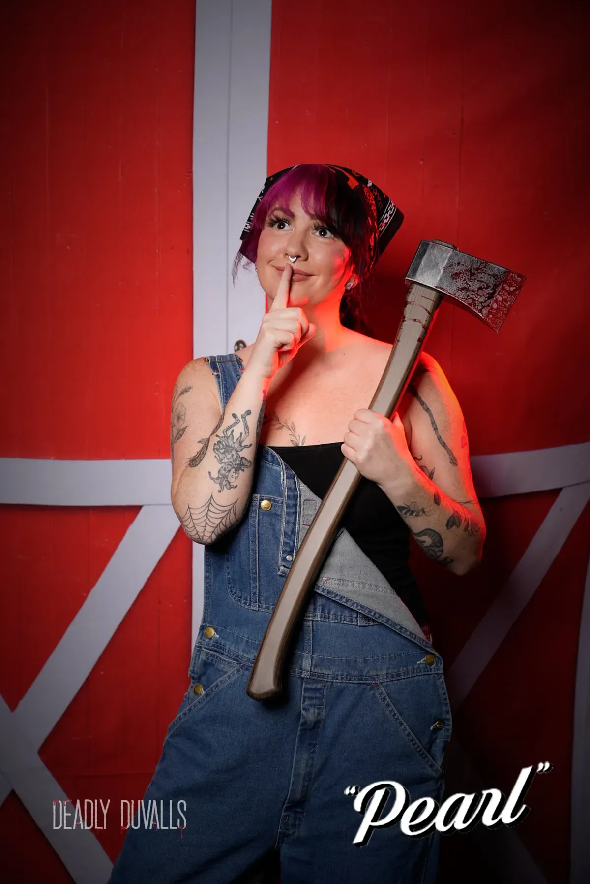 Guest with pink and purple hair in a bandana and denim overalls, finger to her lips holding a bloodied axe, at the Deadly Duvalls Pearl photo booth in Los Angeles