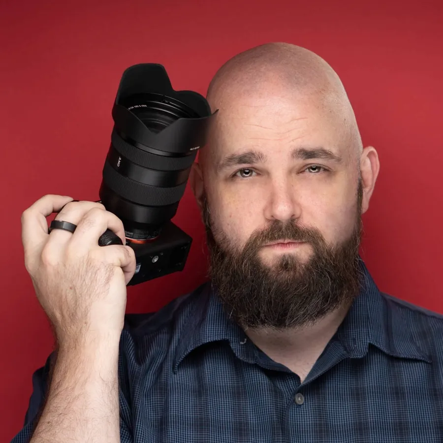 Josh Duvall, horror photographer at Deadly Duvalls, holding a camera against a red backdrop